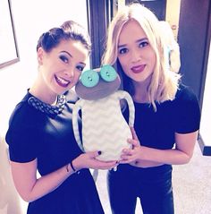 two women standing next to each other holding a stuffed animal in front of the camera