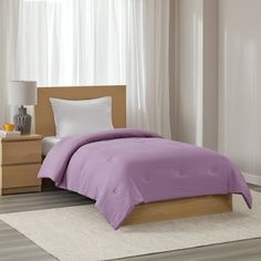 a bed in a bedroom with purple comforter and pillows