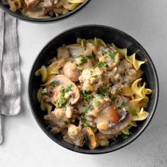 two black bowls filled with pasta and meat covered in mushroom sauce on top of a white table