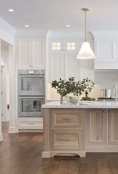 a large kitchen with white cabinets and wood flooring is pictured in this image, there are lights hanging from the ceiling over the island