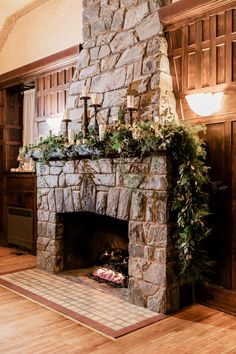 a stone fireplace with candles and greenery on the mantle