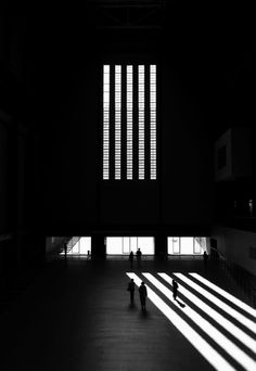 two people standing in the middle of a room with large windows and long shadows on the floor