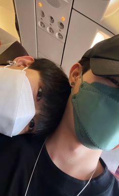 two people wearing masks on an airplane looking down at the camera man and woman are sleeping