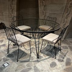 a glass table with four chairs in front of it and a stone wall behind it