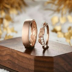 two wedding bands with leaves on them sitting on top of a wooden stand next to each other