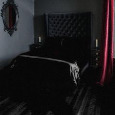 a bed in a dark room next to a window with red drapes on it