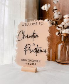 a welcome sign for a baby shower with cotton flowers in a vase and wooden block