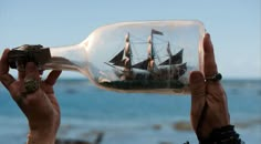 a person holding up a bottle with a ship in it