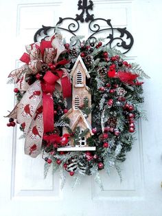 a christmas wreath with a church on it and red bows hanging from the front door