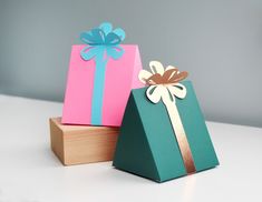 two gift boxes with bows on them sitting next to each other, one is green and the other is pink