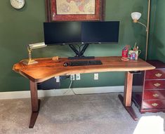 a computer desk with two monitors and a keyboard in front of a painting on the wall