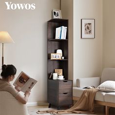 a woman sitting on a couch reading a book in front of a tall wooden shelf