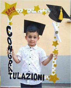 a young boy wearing a graduation cap and gown holding a sign with stars on it