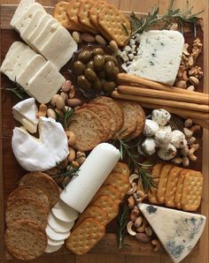 an assortment of cheeses, crackers and nuts on a cutting board with rosemary sprigs