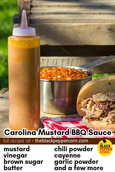 a bbq sandwich with beans and mustard next to a bottle of barbecue sauce on a picnic table