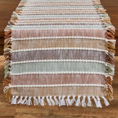 a striped table runner with tassels on top of it, sitting on a wooden floor