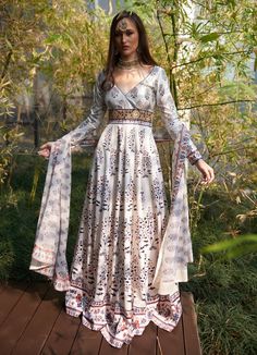 This elegant White Printed Satin Silk Anarkali Gown, crafted from luxurious satin silk, exudes graceful charm with its flowing design and intricate details. The white anarkali showcases mesmerizing printed motifs inspired by traditional patterns, accentuated by delicate waist embroidery for a touch of regal opulence. Featuring a flattering V-neckline and full-length sleeves, the Anarkali flows effortlessly, creating captivating movement with every step. Paired with a comfortable matching churida Floor-length Off White Salwar Kameez For Festivals, Festival Floor-length Off White Salwar Kameez, Off-white Floor-length Salwar Kameez For Festivals, Wedding Lehenga With Printed Motifs, Wedding Lehenga With Printed Motifs In Maxi Length, Floor-length Anarkali Set With Printed Motifs For Wedding, Printed Motifs Floor-length Anarkali Set For Wedding, Off White Anarkali Gown With Dupatta, Bohemian Anarkali Set With Printed Motifs For Wedding