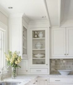 a kitchen with white cabinets and marble counter tops is pictured in this image, there are vases on the window sill