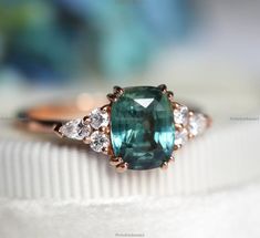 an oval cut green and white diamond ring on top of a white cloth with other jewelry items in the background