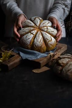 a person holding a loaf of bread on top of a wooden cutting board