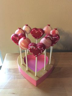 heart shaped lollipops are arranged on sticks in a wooden holder with pink and white icing