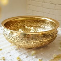 a golden bowl sitting on top of a white table cloth next to a brick wall