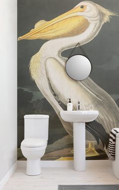 a white toilet sitting next to a bathroom sink under a mirror with a bird painted on it