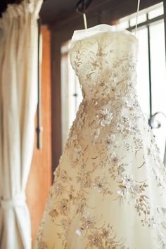 a wedding dress hanging on a rack in front of a window