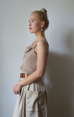 a woman standing in front of a white wall wearing a tan top and beige skirt