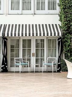 two white chairs sitting in front of a building with black and white striped awnings