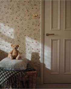 a teddy bear sitting on top of a pillow in front of a wallpapered room