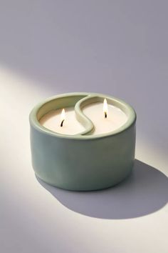 two candles sitting in a green bowl on a white surface