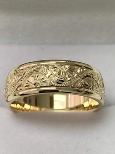 a yellow gold wedding ring with an intricate design on it's side, sitting on a white surface