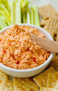 a white bowl filled with dip next to crackers and celery