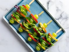 several skewers of vegetables are arranged on a blue platter with grapes and lettuce