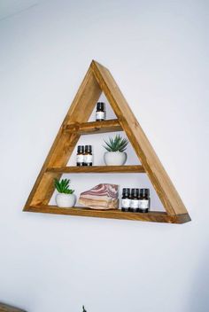 a wooden triangle shelf with bottles and candles on it in front of a white wall