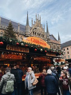 people are standing in line to get food at the german christmas market, with an old building in the background