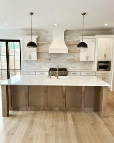 a large kitchen with an island in the middle and two pendant lights hanging from the ceiling