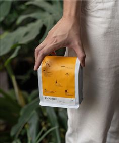 a person holding onto a yellow and white sign in front of some green plants on the ground