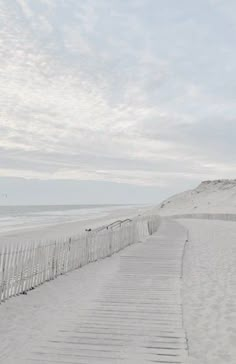 a path leading to the beach with white sand and blue skies in the background on a cloudy day