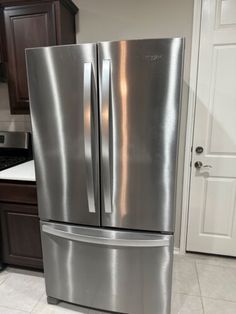 a stainless steel refrigerator in a kitchen with dark wood cabinets and white tile flooring