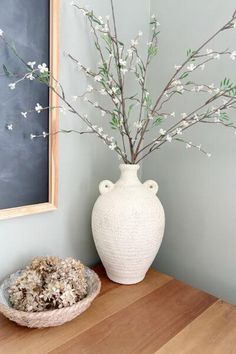 a white vase sitting on top of a wooden table next to a bowl filled with flowers