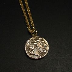 Handmade Zeus pendant by reproducing an ancient Greek coin of Zeus or Jupiter in Latin.The original coin was minted by Philip II (father of Alexander the Great) in Pella, Macedonia between 359 and 336 BC.It represents Zeus, king of the Gods. God of the sky, lightning, thunder, law, order, justice.The quality of Zeus’ particularly elegant portrait on this coin, with a smooth forehead, clean arch of the eyebrow, and finely chiseled nose shows its inspiration by the gold and ivory statue of Zeus by Brass Coin Pendant Necklace For Gift, Ancient Style Brass Necklace With Coin Pendant, Bronze Coin Pendant Necklace, Collectible Spiritual Coin Necklaces, Brass Coin Necklace For Gift, Brass Coin Necklace Gift, Ancient Brass Necklace With Coin Pendant, Bronze Coin Amulet Necklaces, Collectible Coin Shaped Amulet Necklace