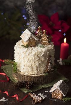 a cake with white frosting and christmas decorations on the table next to a lit candle