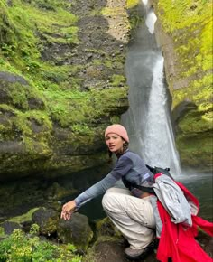 a woman standing in front of a waterfall with backpacks on her back and water running down it