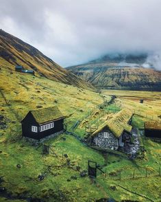 two small houses with grass roofs in the middle of a mountain range on a cloudy day