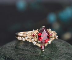 Introducing our Vintage Pear Red Ruby Engagement Ring set, a masterpiece inspired by the allure of nature's intricate beauty. This unique cluster diamond bridal wedding ring set seamlessly blends vintage charm with modern elegance. Ring set comes with the engagement ring and band. By default, the accent stones are set with moissanite accents from VS to VSS clarity. Please contact us if you would like to have this changed to lab grown or natural diamonds. Product Details Pear Red Ruby: The heart Ruby Ring Vintage Red Antique Jewelry, Ruby And Gold Engagement Ring, Red Rings Engagement, Ruby And Gold Ring, Red And Gold Ring, Opal And Ruby Ring, Ruby And Emerald Ring, Engagement Rings With Ruby, Wedding Rings Ruby