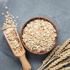 some oats in a bowl next to a wooden spoon and two stalks of wheat