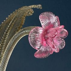 a pink glass flower sitting on top of a metal planter next to a blue wall