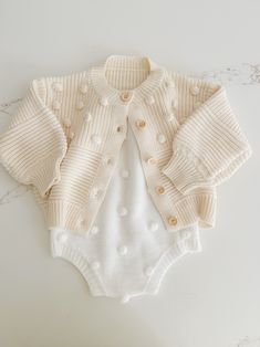 Soft and cozy, this stunning knit cardigan is the perfect addition to your little ones closet. Tiny Pom Pom appliqués all over. Textured pattern with front buttons. Cute Cream Soft Knit Sweater, Playful Knit Long Sleeve Outerwear, White Knit Buttoned Cardigan, Playful Cotton Knitted Cardigan, Playful Knitted Cotton Cardigan, Cute Button-up Sweater For Winter, Cute Winter Button-up Cardigan, Cute Button-up Winter Sweater, Cute Button-up Cardigan For Fall